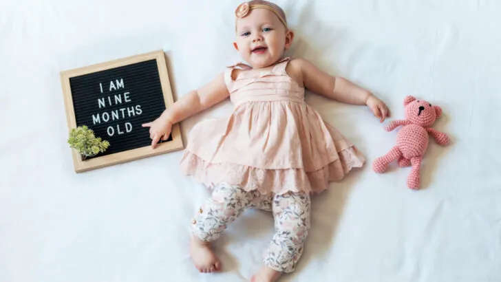 9 month old baby girl lying on blanket with sign that says 