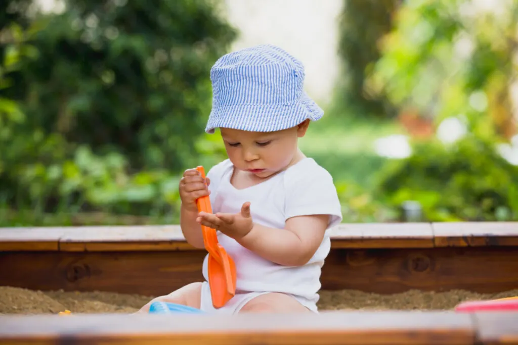 nine month old baby playing in sand box with sand toys.