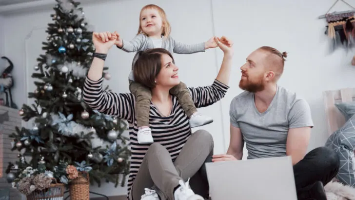 9 month old on mom's shoulders with dad in front of Christmas tree