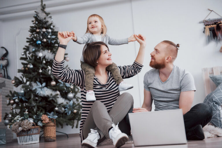 9 month old on mom's shoulders with dad in front of Christmas tree