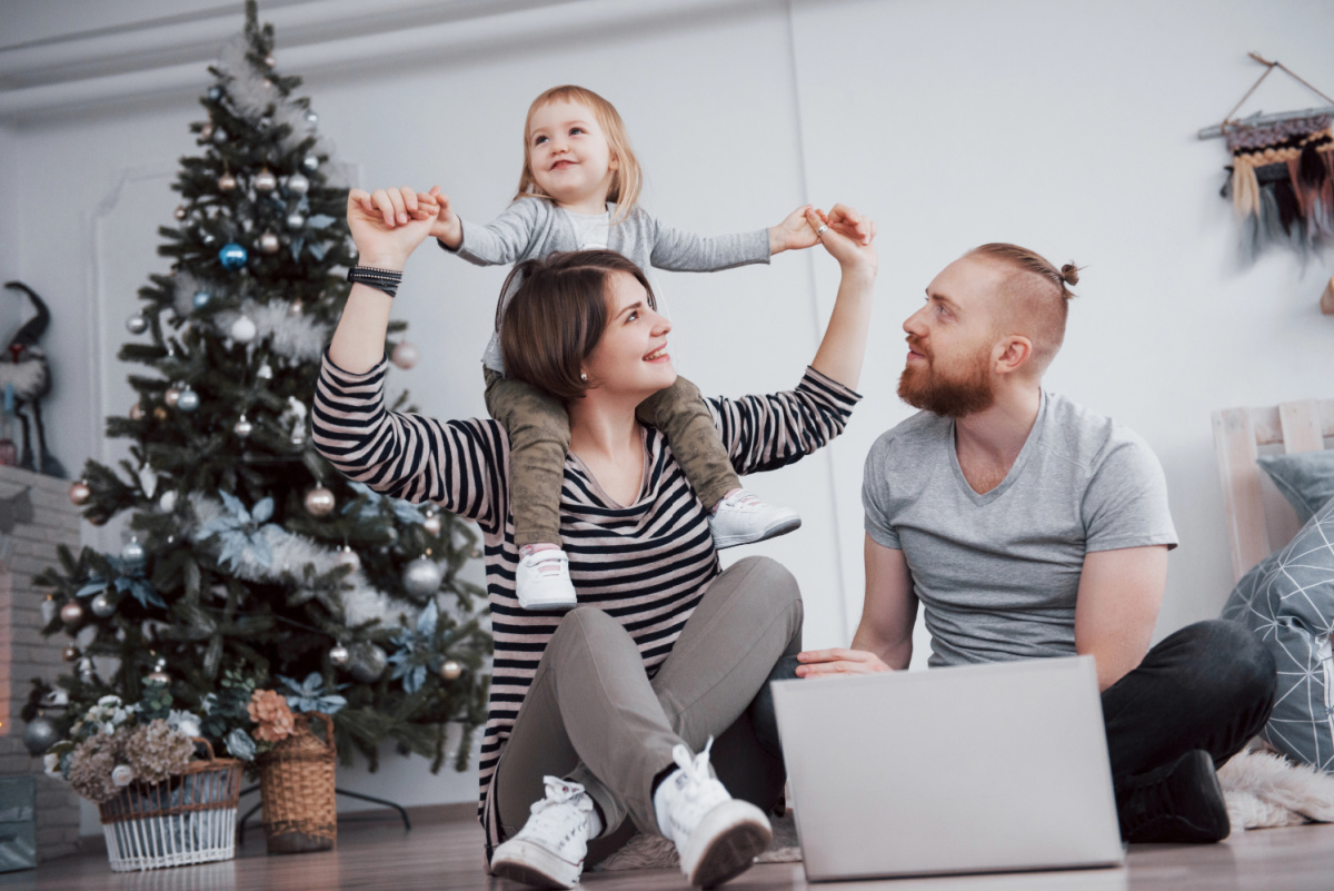 9 month old on mom's shoulders with dad in front of Christmas tree