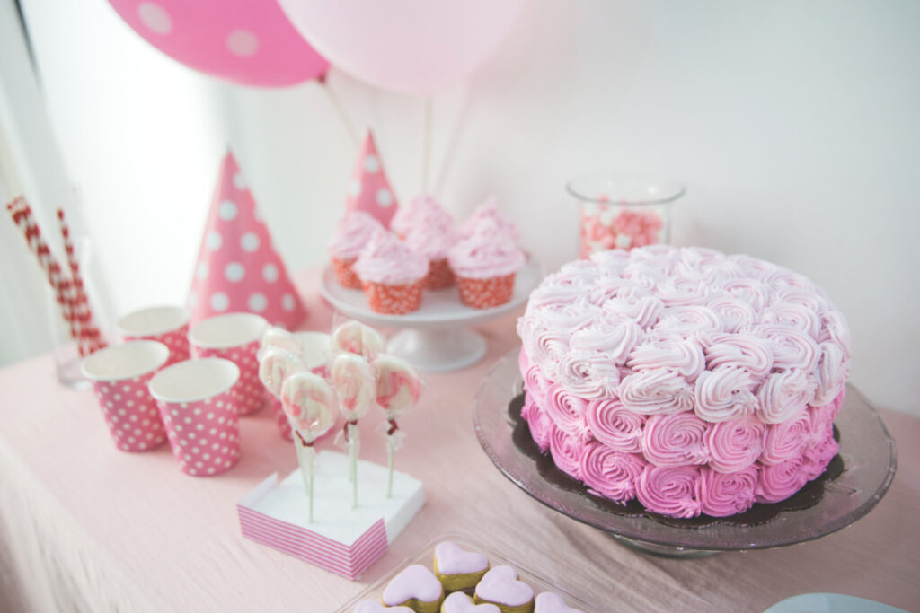 baby shower pink cake with rose swirls, cupcakes and lollypops nearby.