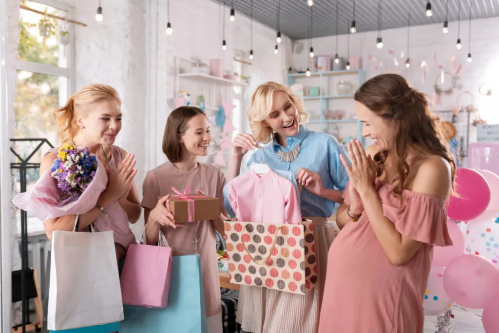 group of women at a baby shower showing gifts to the mom-to-be.