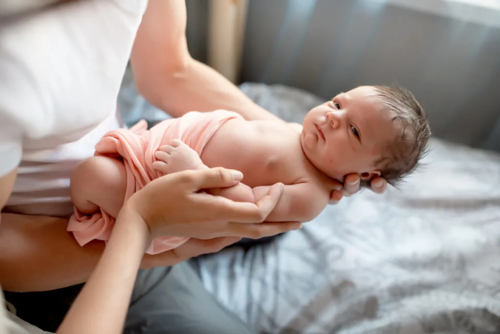 newborn in peach-colored swaddle blanket, being held by dad.