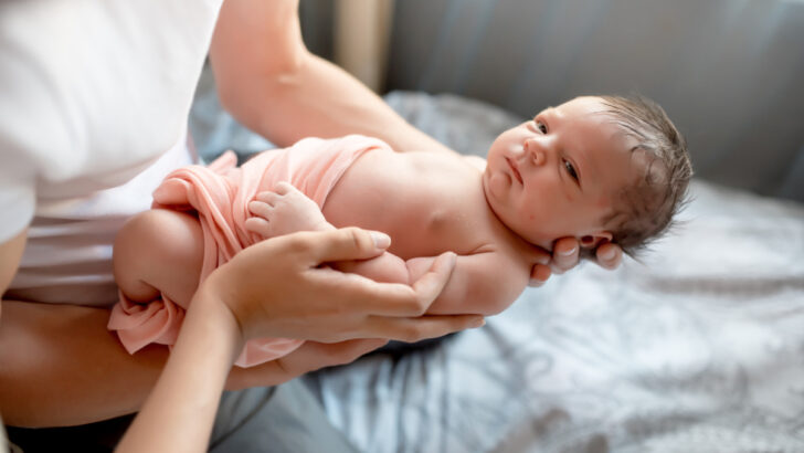 newborn in peach-colored swaddle blanket, being held by dad.