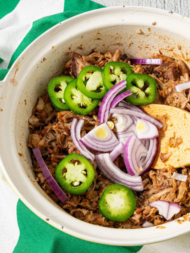 dutch oven carnitas with fresh jalapeños and red onions on top.