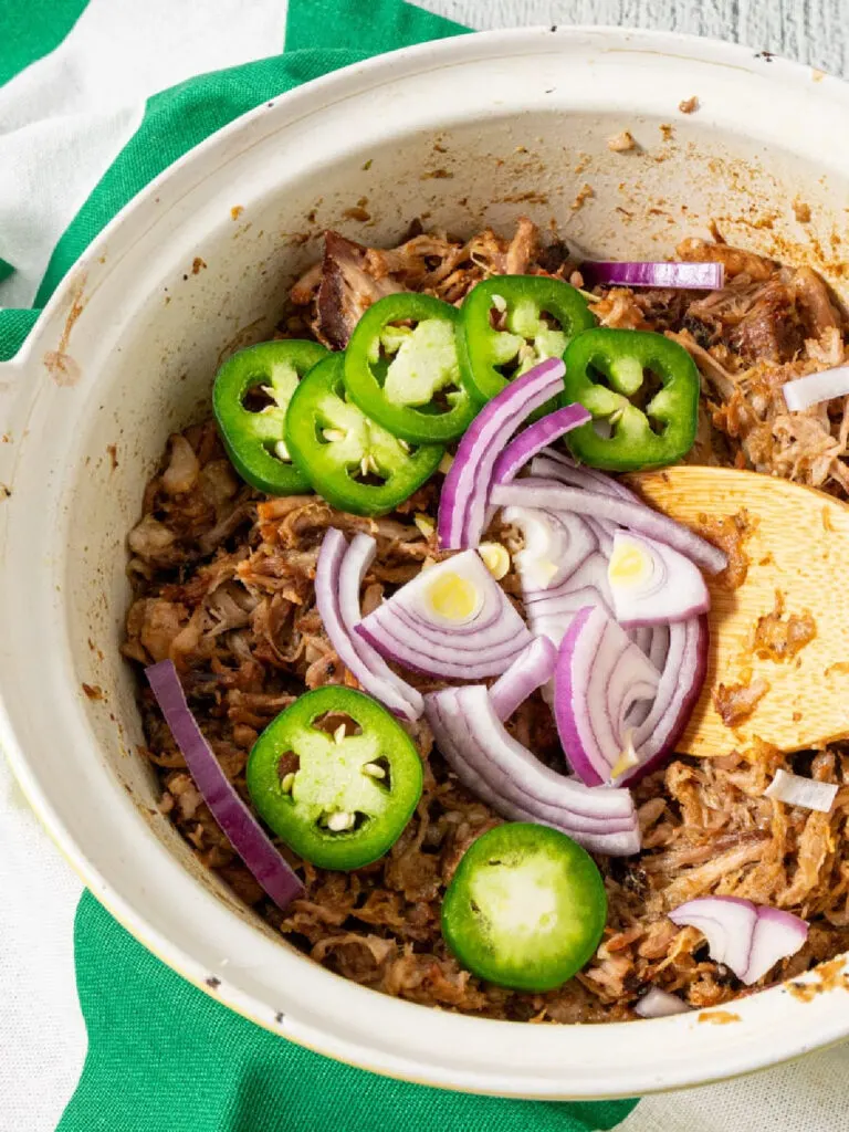 dutch oven carnitas with fresh jalapeños and red onions on top.