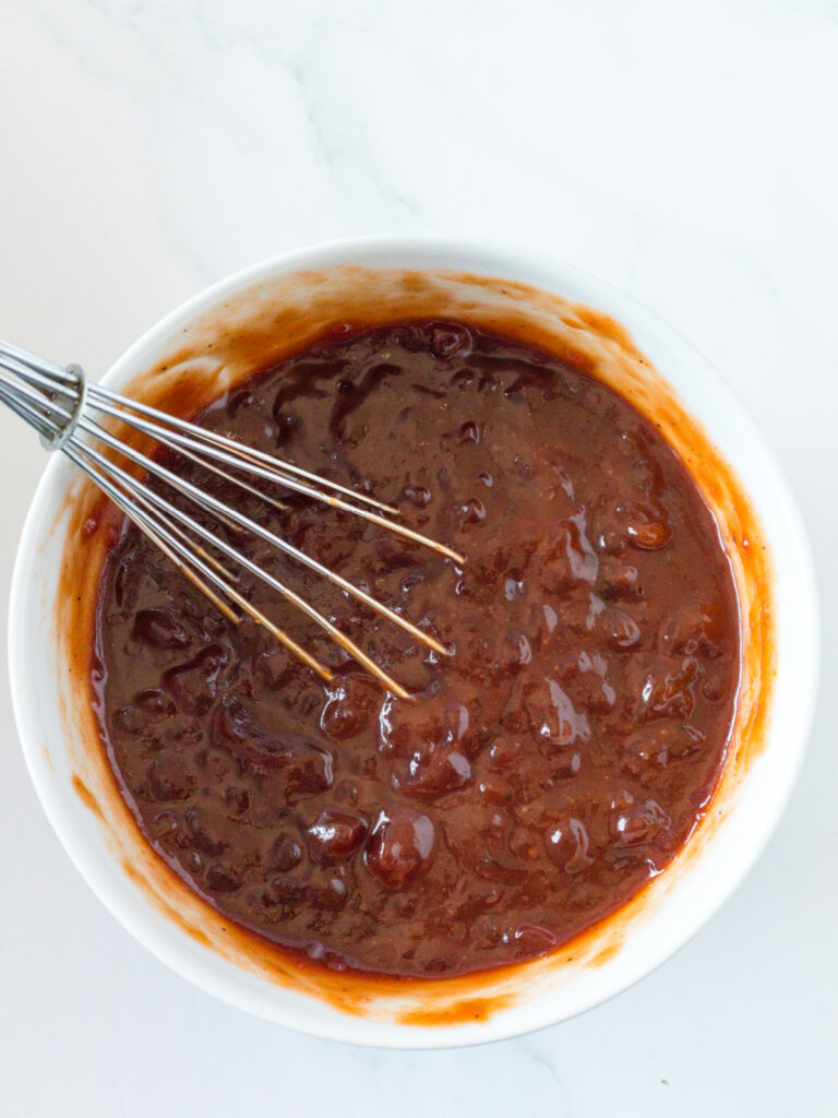 sauce for crockpot cranberry BBQ meatballs in white bowl with whisk.
