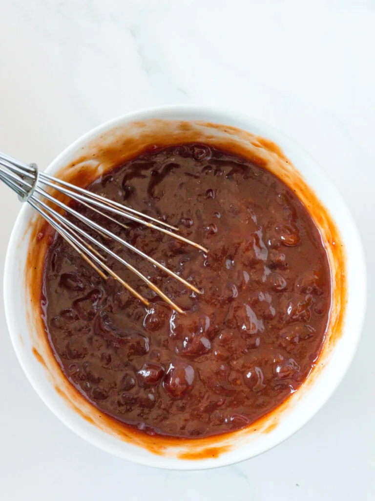 sauce for crockpot cranberry BBQ meatballs in white bowl with whisk.