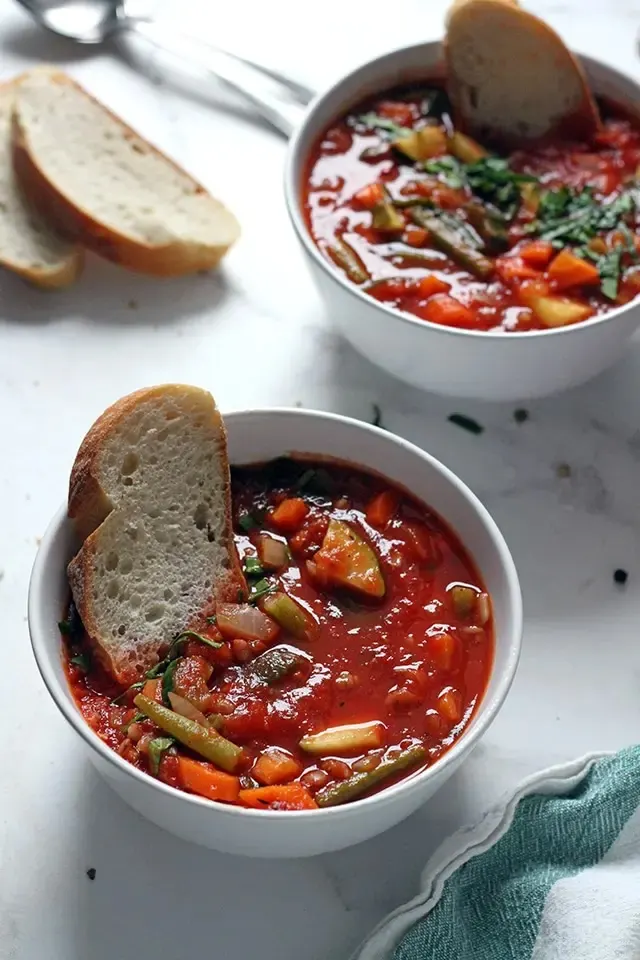 vegan minestrone in white bowl with spoon.