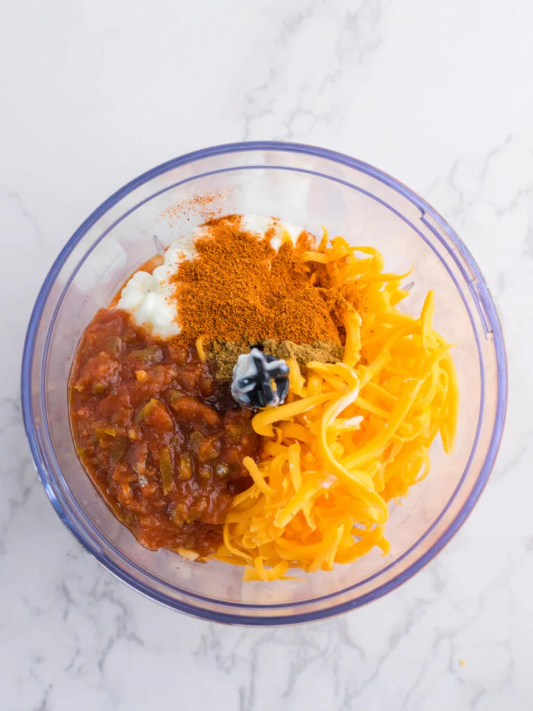 ingredients for cottage cheese queso dip in food processor on marble countertop.