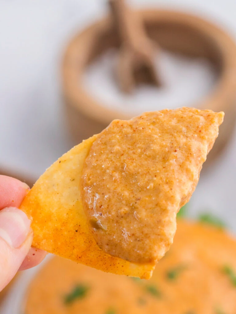 tortilla chip with cottage cheese queso dip on top in focus.