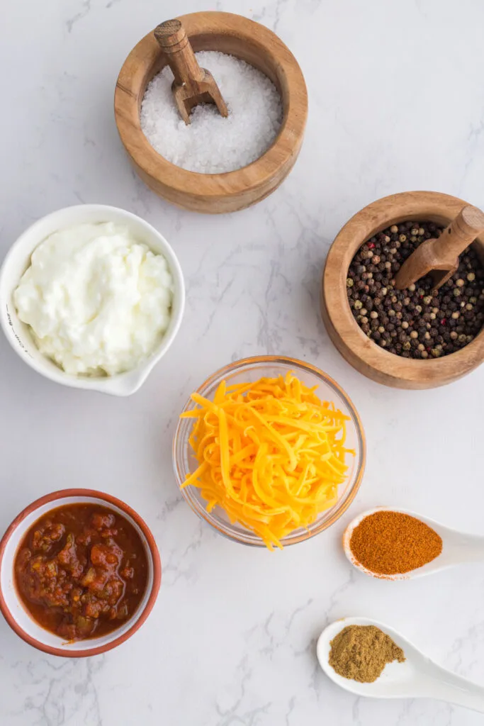 ingredients for cottage cheese queso dip in small bowls and measuring spoons on marble countertop.