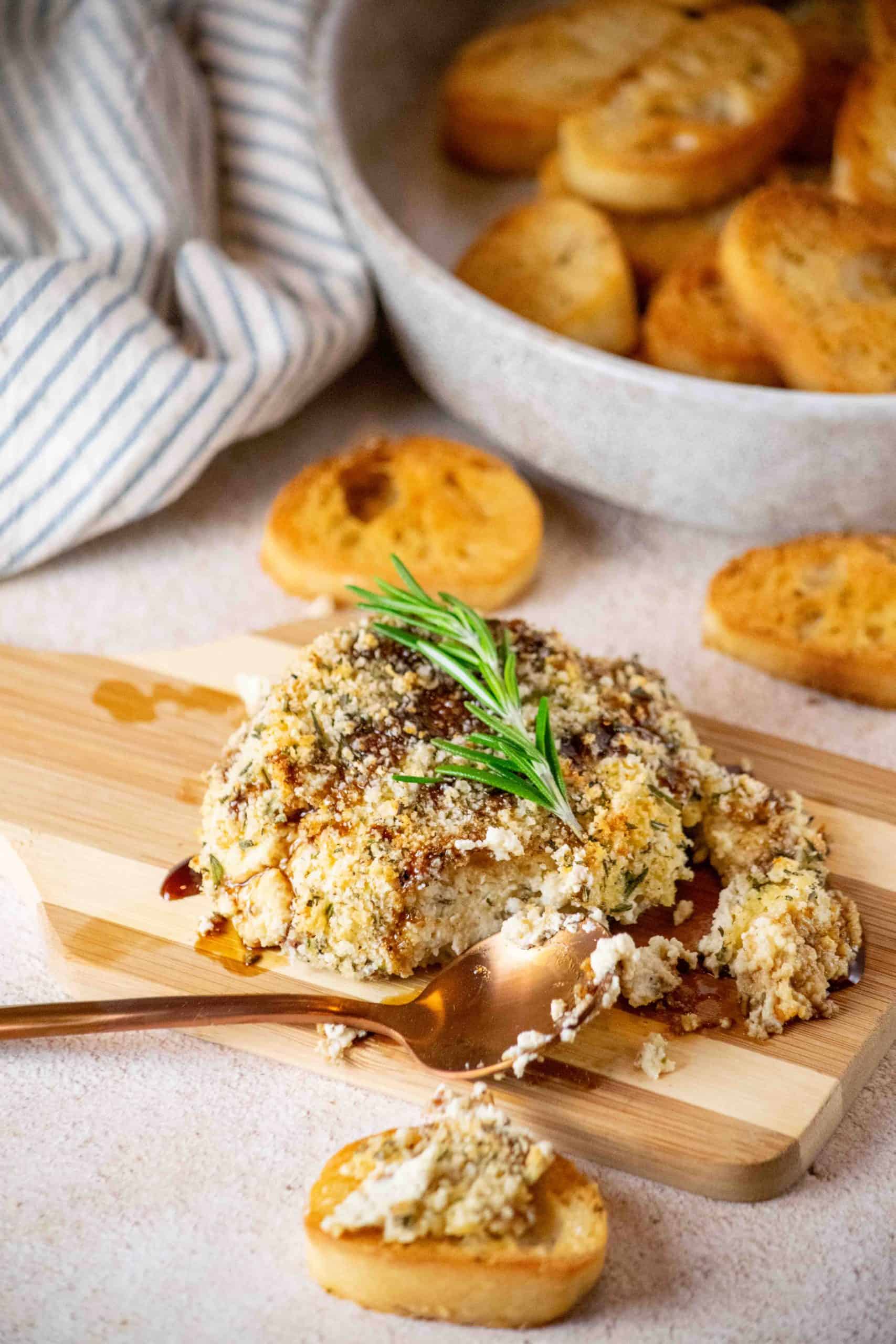 baked Boursin cheese with pomegranate molasses on cutting board with crostini in the background.