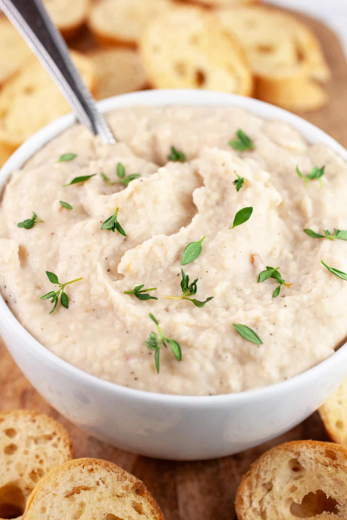 Italian white bean dip in white bowl with spoon and sliced baguette in background.