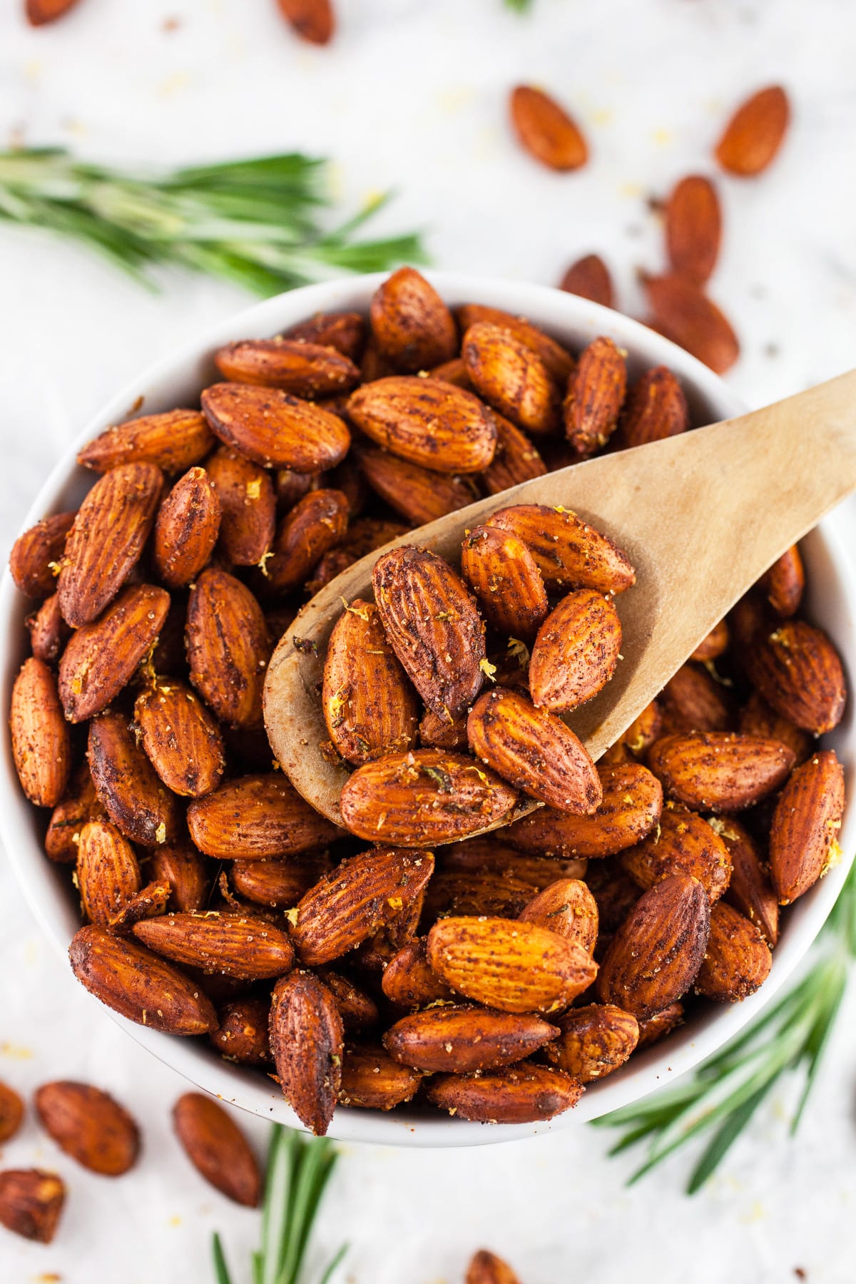 rosemary roasted almonds in white bowl with wooden spoon scooping them up.