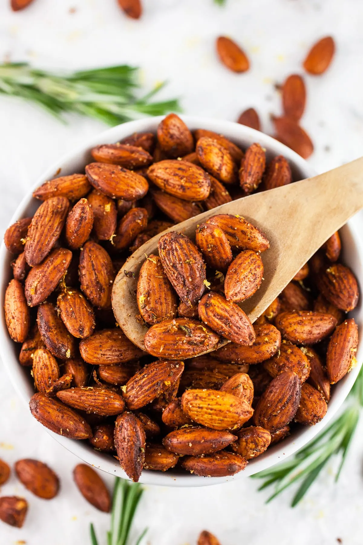 rosemary roasted almonds in white bowl with wooden spoon scooping them up.