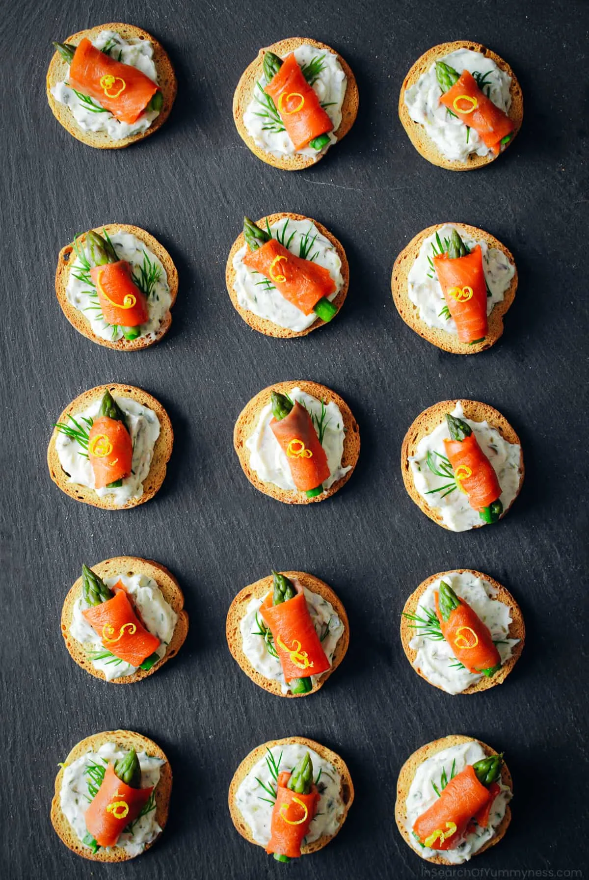 salmon crostini appetizers assembled and lined up on black countertop.