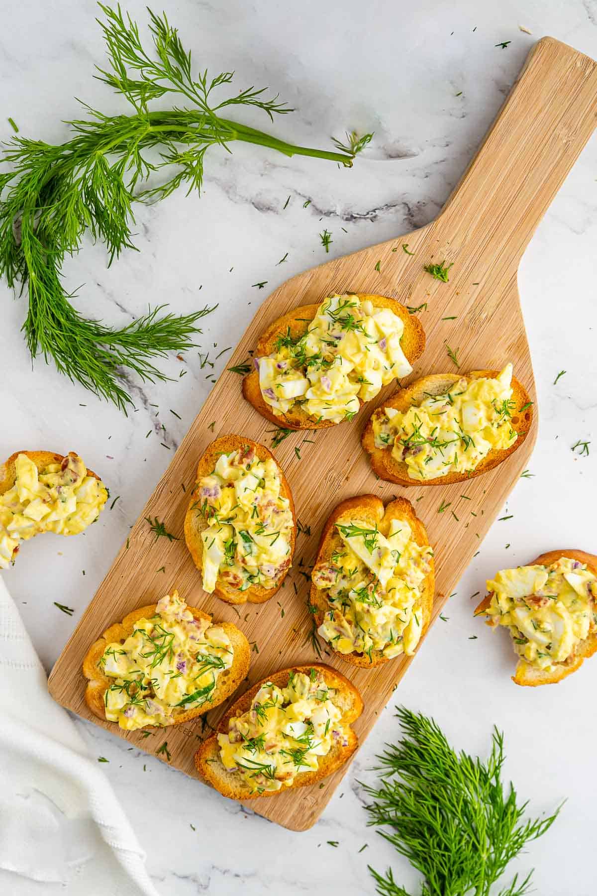 bacon and egg crostinis on cutting board with fresh sprigs of dill on the side.