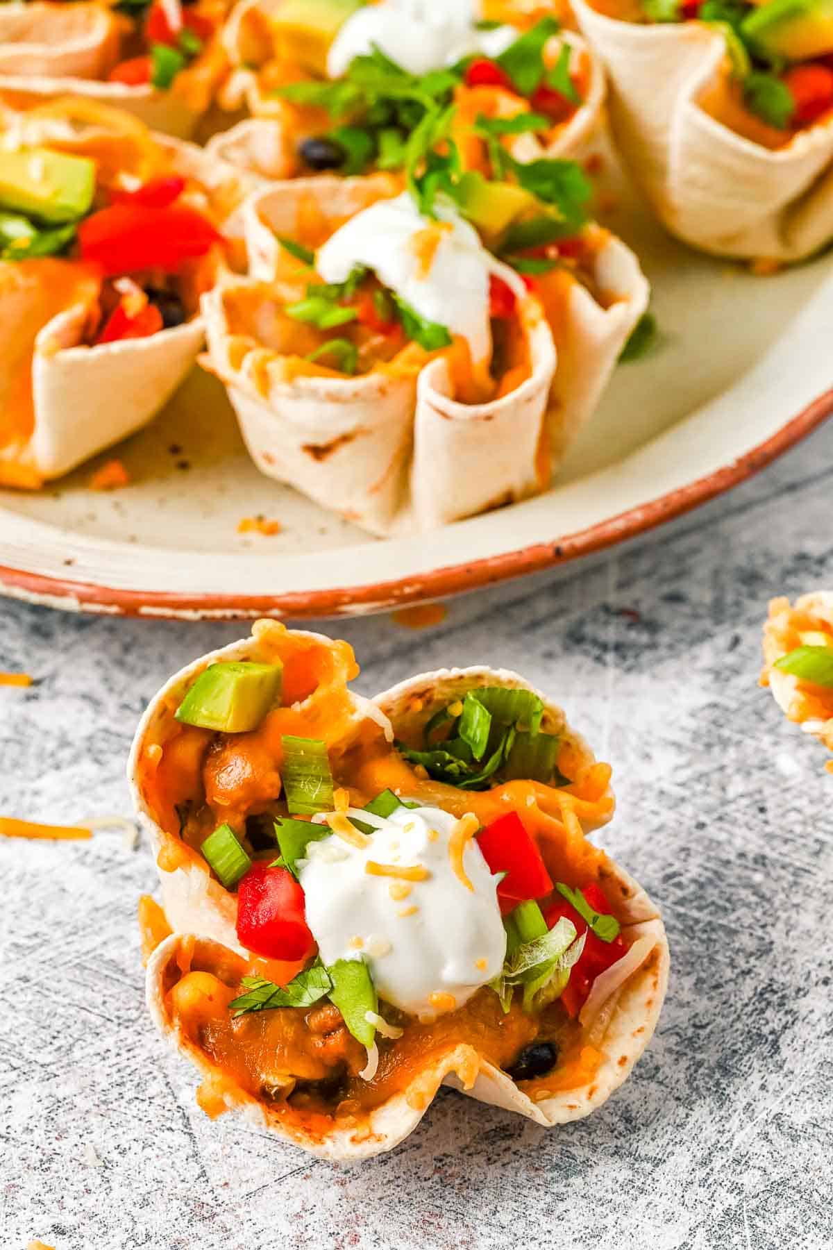 easy enchilada cup appetizers on a platter with single cup in focus.