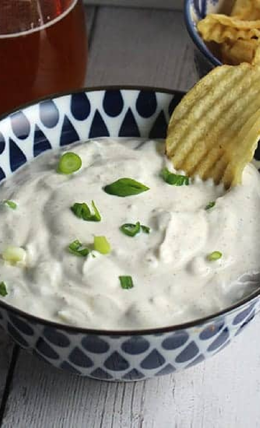 spicy green onion dip in white and blue bowl with ruffles chip in dip.