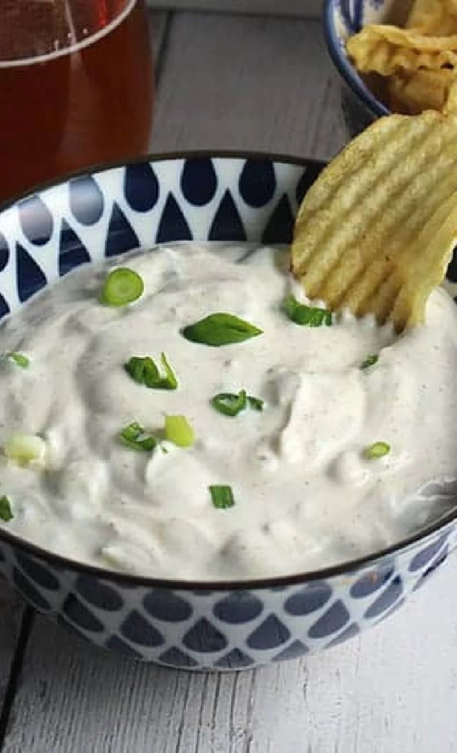 spicy green onion dip in white and blue bowl with ruffles chip in dip.